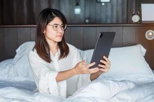 Happy woman using tablet for video call, female meeting  online by computer pad on bed. technology, network, work from home, lifestyle and digital communication concept photo