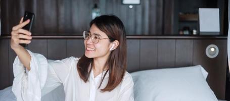 Happy woman using smart phone for video call, female meeting  online by mobile phone on bed. technology, network, work from home, lifestyle and digital communication concept photo