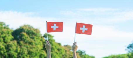 hand holding Switzerland flag on blue sky background. Switzerland National Day and happy celebration concepts photo