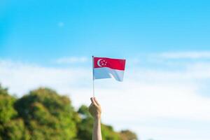 mano sosteniendo la bandera de singapur sobre fondo de cielo azul. día nacional de singapur y conceptos de celebración feliz foto