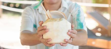 Man holding fresh coconut juice during drinking on tropical beach. Summer, relaxing and vacation concepts photo