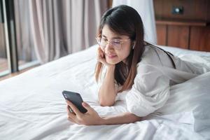 woman using smartphone for social media, young female watching movies by mobile phone on bed at home. technology, network, online shopping, e commerce, lifestyle and digital communication concept photo