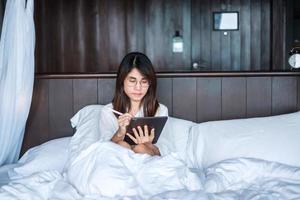 Happy woman using tablet for social media, young female watching movies on computer pad on bed at home. technology, network, online shopping, e commerce, lifestyle and digital communication concept photo