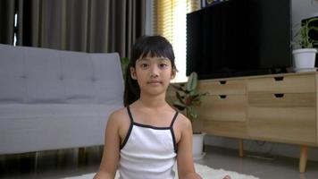 niña asiática sentada en la alfombra y coloca la mano en la rodilla abre los ojos después de la pose de meditación en casa video