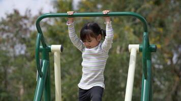Aziatisch meisje geniet ervan om met een glimlach op fitnessapparatuur buiten te spelen, op de speelplaats video