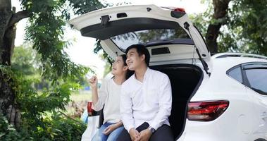 retrato de una feliz pareja asiática sentada y mirando la vista en la parte trasera de un auto. concepto de viaje y estilo de vida. video