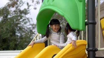Cute older sister and youngest sitting talking and laugh with fun on the slider in playground video