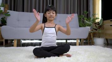 slow motion-bild, liten asiatisk flicka som sitter på mattan stängde ögat och placerade två händer på bröstet i meditationsasanaställning hemma video