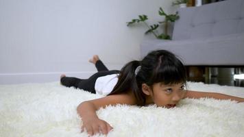 niña asiática tendida en la alfombra cansada después de jugar gimnasia con postura de arco, use el pie para tocar su cabeza en la alfombra en la sala de estar en casa video