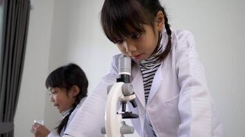 Slow motion shot, Two asian siblings wearing coat use microscope for experimenting with liquids, while studying science chemistry, selective focus video