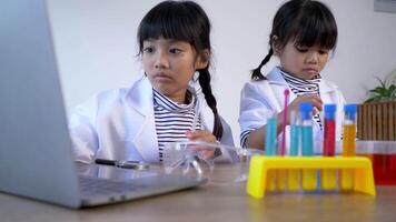 Slow motion shot, Two asian siblings wearing coat use laptop computer for experimenting with liquids, while studying science chemistry, selective focus video