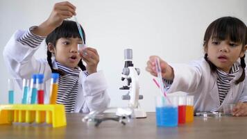 Two Asian siblings wearing coat are using the device for experimenting with liquids. They talking while studying science chemistry with fun video