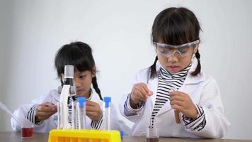 twee Aziatische broers en zussen met een jas en een doorzichtige bril gebruiken het apparaat om met vloeistoffen te experimenteren. tijdens het studeren van scheikunde video