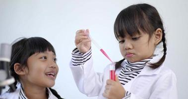 Slow motion shot, little girl use dropper liquid on plate test, Two asian siblings wearing coat learning experimenting with liquids, while studying science chemistry with fun video