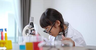 jolie fille à lunettes sourire avec plaisir, utiliser un microscope, un ordinateur portable et un appareil d'expérimentation de liquides sur table, tout en étudiant la chimie scientifique, mise au point sélective video