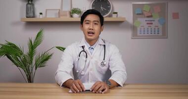 Portrait of young asian male doctor with stethoscope makes online video call consult patient and looks at camera. Medical assistant therapist videoconferencing. Telemedicine pandemic concept.