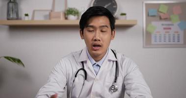 Portrait of young asian male doctor with stethoscope makes online video call consult patient and looks at camera. Medical assistant therapist videoconferencing. Telemedicine pandemic concept.