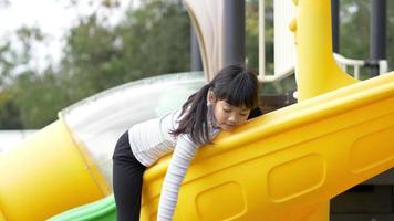 Handheld shot, Portrait Asian little girl sitting on slider and play alone in playground