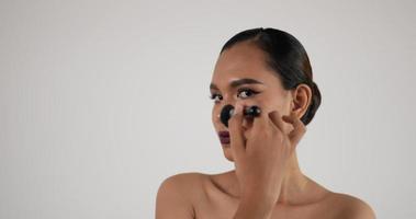 El primer plano de una mujer asiática de belleza hace maquillaje con un fondo blanco aislado. bella modelo femenina se ruboriza en la cara usando un pincel de maquillaje. concepto de anuncios cosméticos. video
