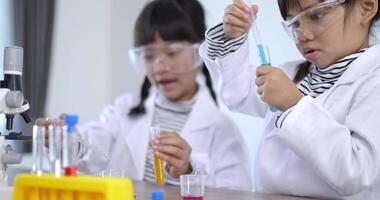 Selective focus, Two asian siblings wearing coat and clear glasses use microscope for experimenting with liquids, while studying science chemistry video