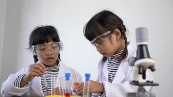 deux frères et sœurs asiatiques portant un manteau et des lunettes transparentes utilisent l'appareil pour expérimenter des liquides. tout en étudiant la chimie des sciences