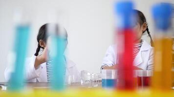 vista dall'alto, due fratelli asiatici che indossano un cappotto in grembo, la ragazza usa il contagocce per aspirare il liquido dal bicchiere di vetro al liquido blu sulla capsula di Petri, studiando la chimica scientifica con divertimento video