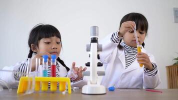 Two Asian siblings wearing coat and clear glasses are using the device for experimenting with liquids. They talking while studying science chemistry with fun video