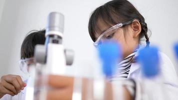 Close up shot, Two Asian siblings wearing coat and clear glasses are using the device for experimenting with liquids. while studying science chemistry video