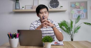 retrato do empresário asiático pensativo trabalhando no computador portátil no escritório em casa. jovem gerente masculino olhando na tela do laptop no local de trabalho remoto.