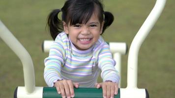Draufsichtaufnahme, asiatisches kleines Mädchen spielt gerne auf Outdoor-Trainingsgeräten mit einem Lächeln auf dem Spielplatz video