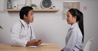 Portrait of young Asian doctor and patient sitting and discussing health examination results in clinic office. Charming male doctor giving advice to a female patient. Medical and health care concept. video