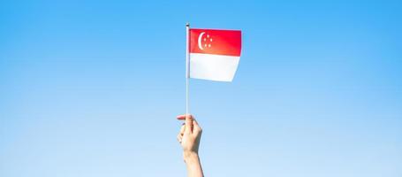 mano sosteniendo la bandera de singapur sobre fondo de cielo azul. día nacional de singapur y conceptos de celebración feliz foto