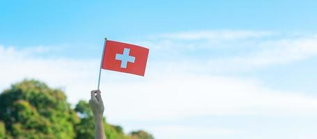 hand holding Switzerland flag on blue sky background. Switzerland National Day and happy celebration concepts photo