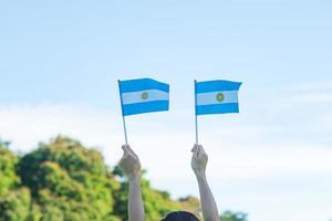 mano sosteniendo la bandera argentina en el fondo de la naturaleza. 9 de julio del día de la independencia, 25 de mayo del día de la revolución y conceptos de celebración feliz foto