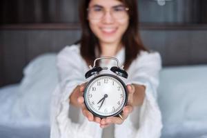 Woman holding alarm clock on bed, happy female wake up in the morning. daily routine, sleep, relaxing and have a nice day concepts photo