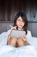 Happy woman using tablet for social media, young female watching movies on computer pad on bed at home. technology, network, online shopping, e commerce, lifestyle and digital communication concept photo