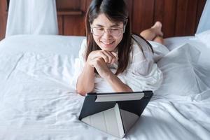 Happy woman using tablet for social media, young female watching movies on computer pad on bed at home. technology, network, online shopping, e commerce, lifestyle and digital communication concept photo