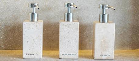 Toiletries bottles in bathroom at luxury hotel or modern home. shower container set, body shower gel, shampoo and hair conditioner in ceramic ware with wall background photo
