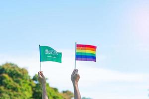 hands showing LGBTQ Rainbow and Saudi Arabia flag on nature background. Support Lesbian, Gay, Bisexual, Transgender and Queer community and Pride month concept photo