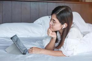 Happy woman using tablet for social media, young female watching movies on computer pad on bed at home. technology, network, online shopping, e commerce, lifestyle and digital communication concept photo