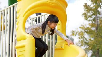 toma manual, retrato de una niña asiática sentada en un deslizador y jugando sola en el patio de recreo video