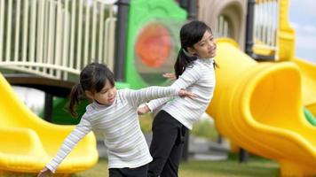 slow-motion shot, twee aziatische schattige meisjes spelen langzaam met de armen uit te strekken en samen gelukkig te glimlachen op de speelplaats video