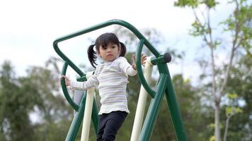 la bambina asiatica si diverte a giocare su attrezzature per esercizi all'aperto con un sorriso al parco giochi video