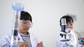 Close up shot, Two Asian siblings wearing coat and clear glasses are using the device for experimenting with liquids. while studying science chemistry video