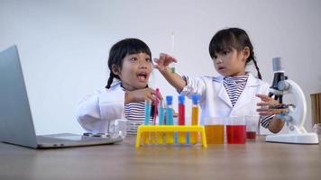 Slow motion shot, Two asian siblings wearing coat use laptop computer for learning and experimenting with liquids, while studying science chemistry, selective focus