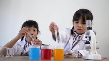 Top view shot, Two Asian siblings wearing coat are using the device for experimenting with liquids. They talking while studying science chemistry with fun
