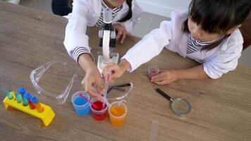 Top view shot, Asian little girl wearing coat using dropper to suck liquid from glass beakers. while studying science chemistry video