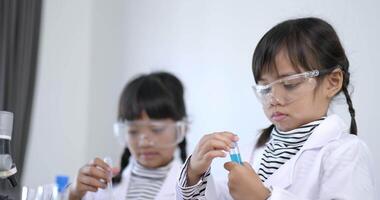 Slow motion shot, Two asian siblings wearing coat and clear glasses use microscope for experimenting with liquids, while studying science chemistry video