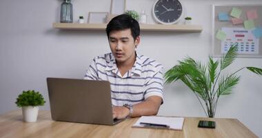 porträtt av glad asiatisk affärsman med bärbar dator som arbetar på hemmakontoret och får goda nyheter på e-post. glada manliga vinnare njuta av framgång på hemmakontoret. video