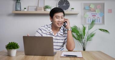 retrato de feliz empresário asiático falando telefone no escritório em casa. jovem empresário usando telefone celular. profissional sorridente conversa no smartphone. video